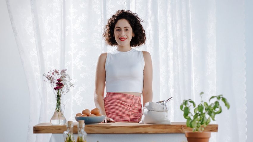 Cheerful woman with curly hair preparing fresh ingredients in a sunlit kitchen setting.